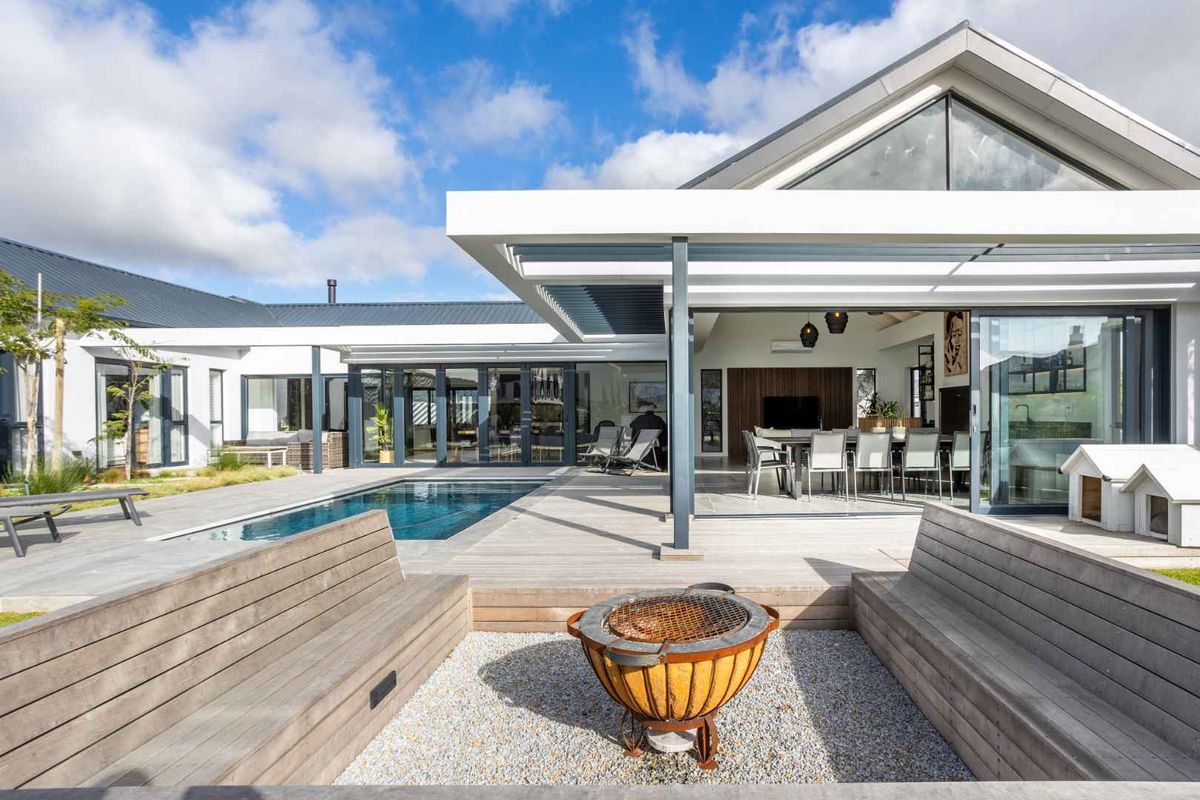 Modern outdoor entertainment area featuring a swimming pool, expansive timber decking, and a sunken fire pit area with built-in timber seating.