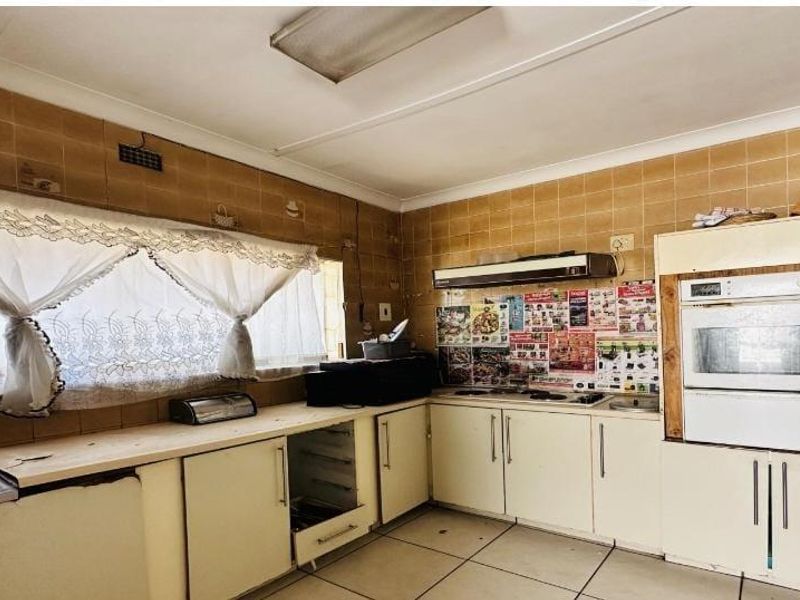 A dated kitchen featuring built-in cabinetry, an integrated oven, hob, extractor fan, and tiled splashbacks, offering significant potential for a modern renovation.