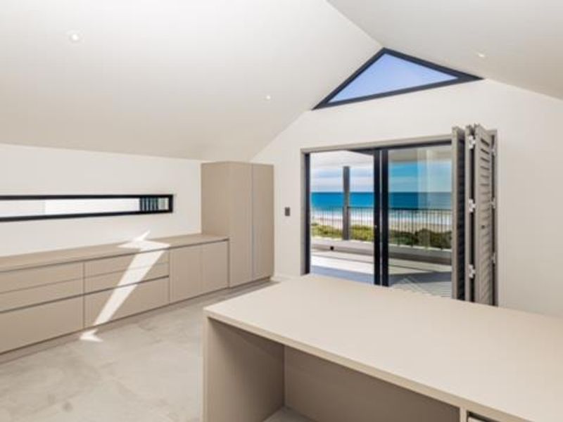 Modern home office featuring built-in cabinetry, vaulted ceilings, and bi-fold doors opening to a balcony with ocean views.
