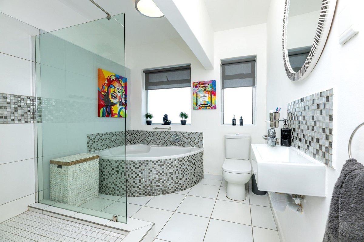Modern bathroom featuring a glass-enclosed shower, a corner bathtub with mosaic tiling, a wall-mounted basin, and neutral ceramic floor tiles.