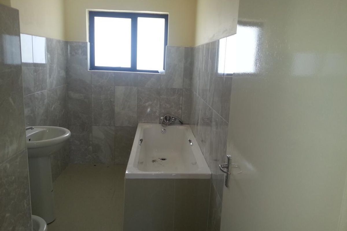A functional bathroom featuring a built-in bathtub, pedestal basin, and grey wall tiling throughout.