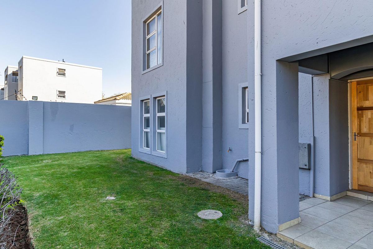 Rear view of the apartment featuring a private garden, tiled patio area, and access through a wooden door.
