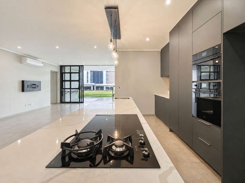 Modern open-plan kitchen featuring a large stone island with gas cooktop, sleek integrated cabinetry, built-in ovens, and seamless flow to the outdoor area.