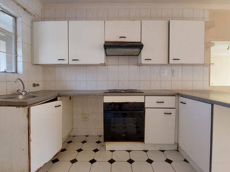 A dated kitchen featuring white cabinetry, laminate countertops, and a built-in oven and hob, offering significant potential for modernization and renovation.