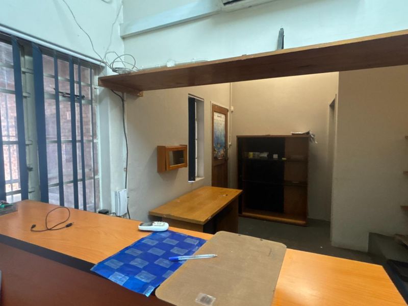 Functional office space featuring a built-in reception counter, integrated shelving units, and security bars on windows, suitable for administrative or industrial operations.