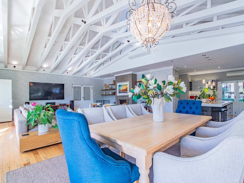 Spacious open-plan living and dining area featuring vaulted ceilings with exposed trusses, hardwood floors, a built-in fireplace, and a modern kitchen.