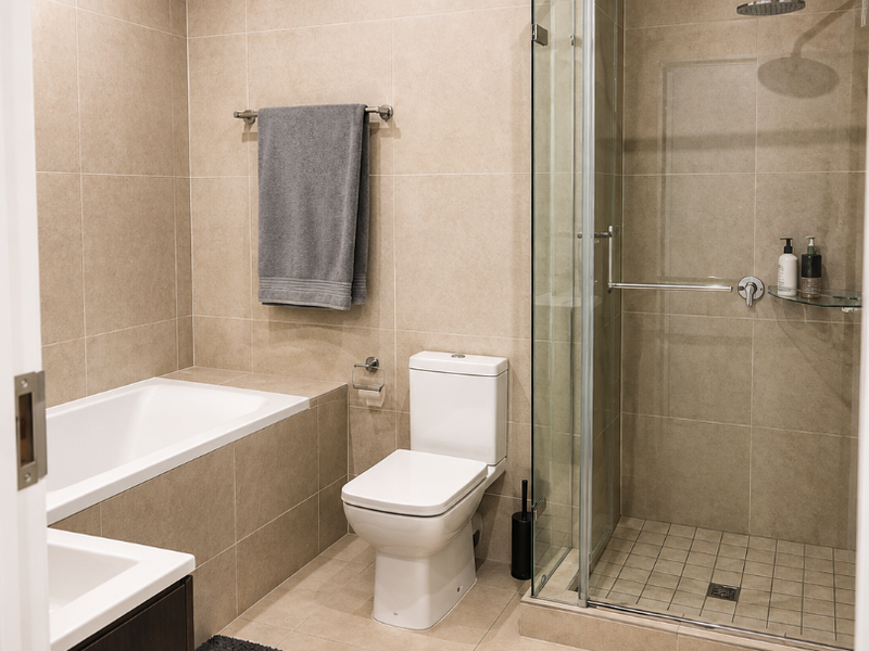 Modern bathroom featuring a built-in bathtub, separate glass-enclosed shower with rain shower head, wall-mounted toilet, and vanity cabinet with neutral floor-to-ceiling tiling.