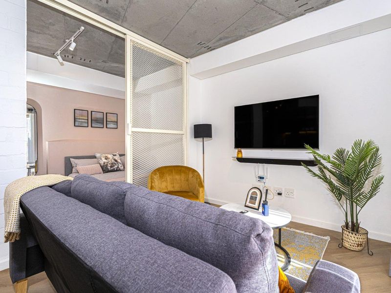Modern living area featuring an exposed concrete ceiling, laminate flooring, and a stylish metal mesh room divider separating the space.