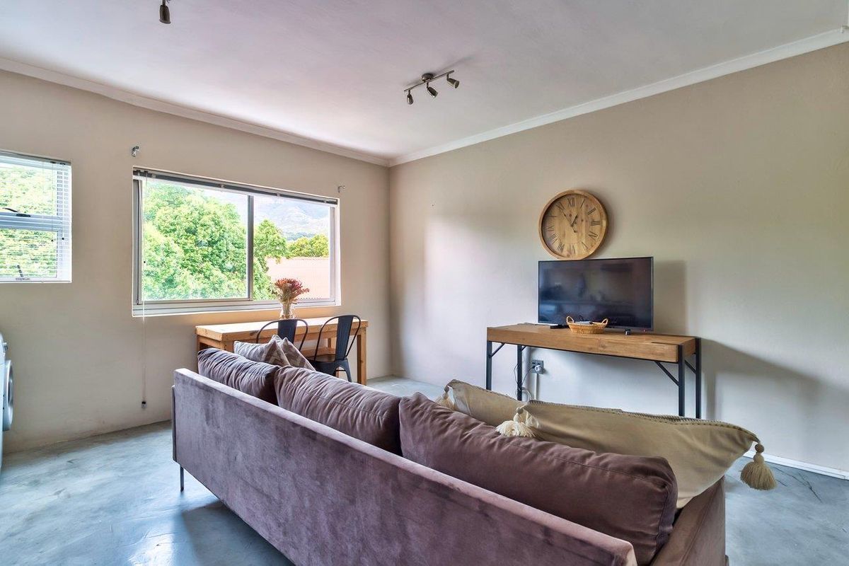 A bright living room featuring polished concrete floors, neutral walls, and large windows providing natural light and a pleasant outdoor view.