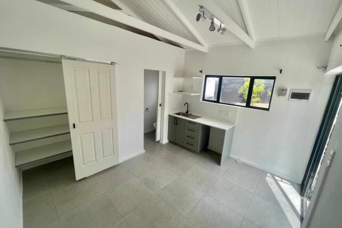 A bright, modern studio kitchen featuring vaulted ceilings, tiled floors, built-in cabinetry with a sink, and a convenient sliding door storage closet.