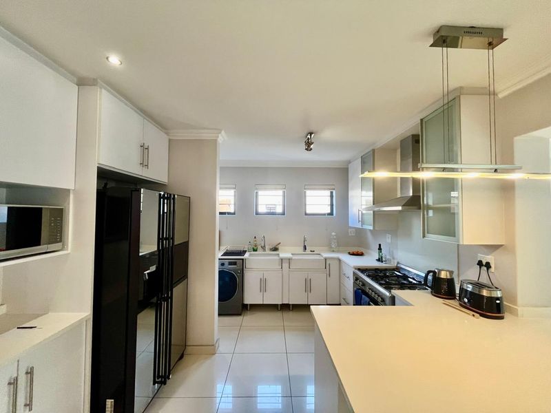 Modern kitchen featuring white cabinetry, stone countertops, a gas hob with extractor, and a double farmhouse sink with tiled flooring.