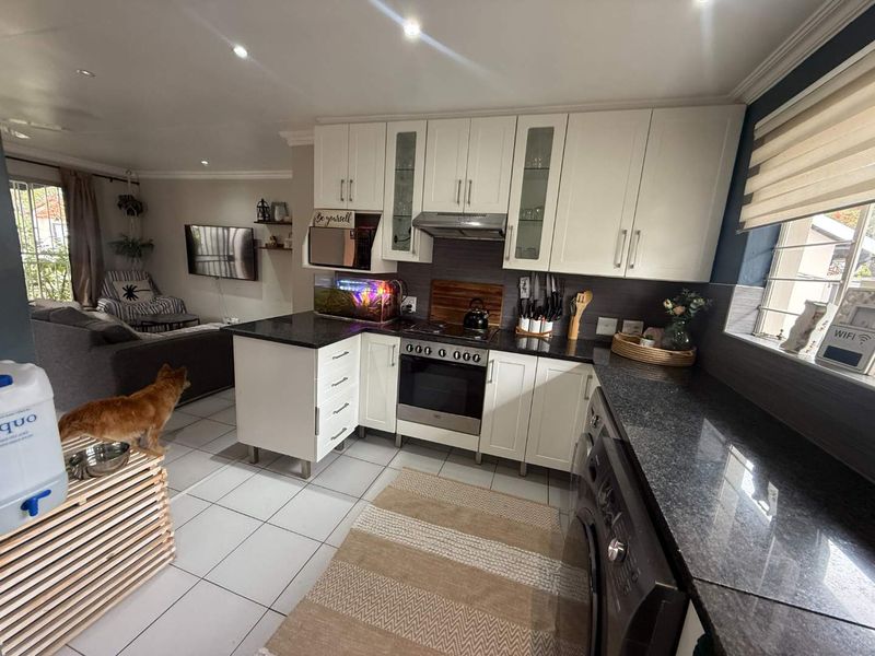 Open-plan kitchen featuring white cabinetry, granite countertops, and integrated appliances, seamlessly flowing into the adjacent living area with tiled flooring throughout.