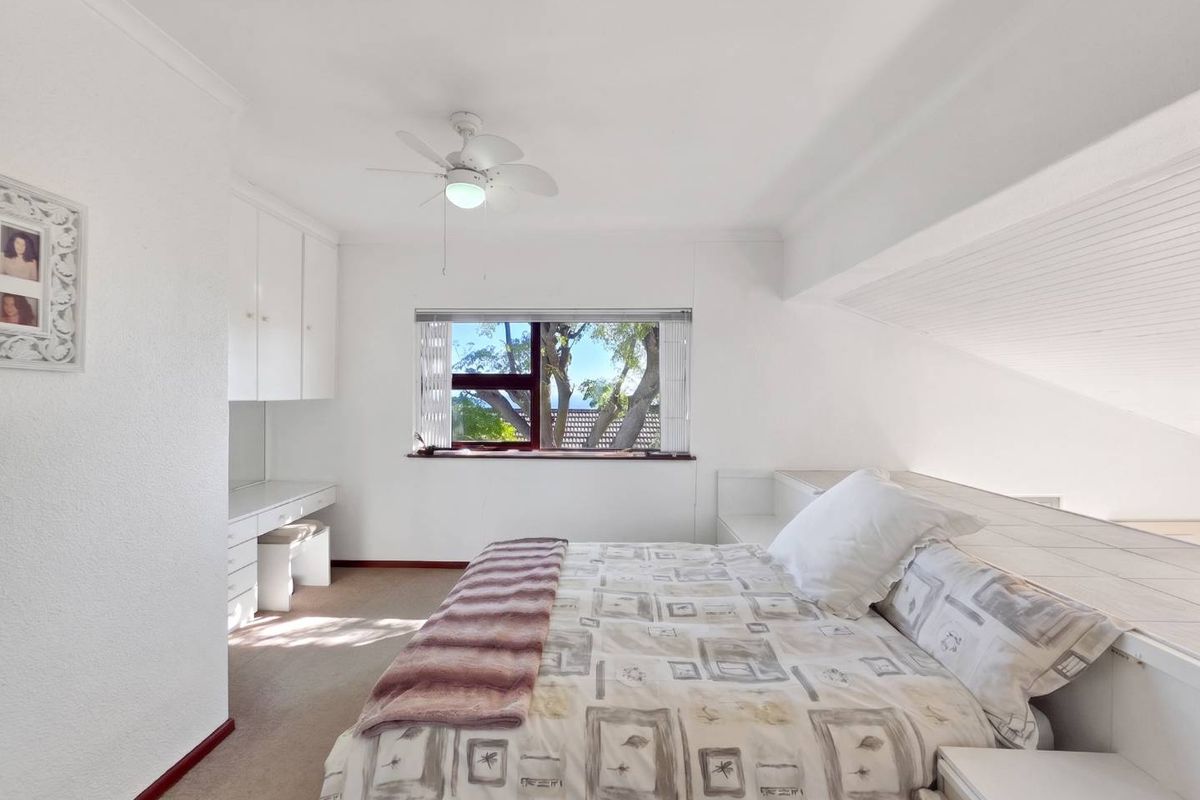A bright bedroom featuring a sloped ceiling, built-in cabinetry, a desk area, and a ceiling fan, offering a functional and comfortable living space.