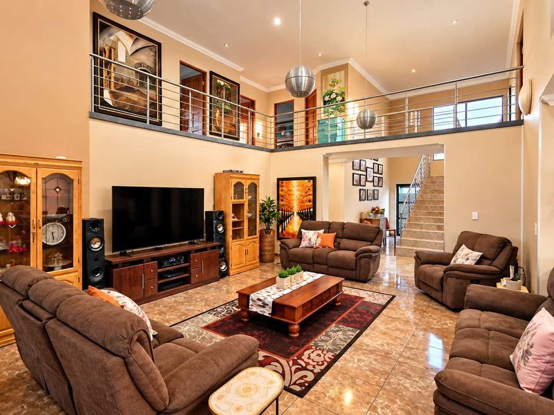 Spacious double-volume living room featuring tiled flooring, a mezzanine level with a stainless steel balustrade, and an open-plan staircase.