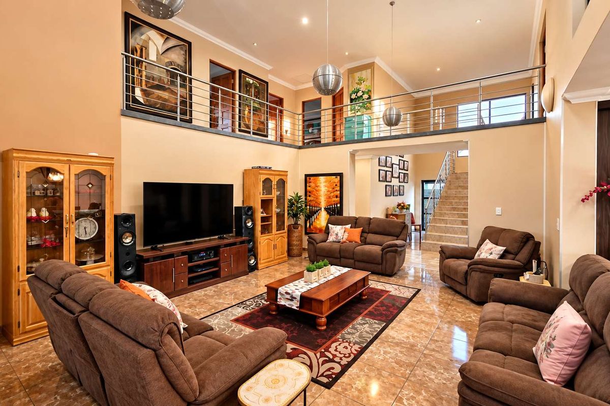 Spacious double-volume living room featuring tiled flooring, a mezzanine level with a stainless steel balustrade, and an open-plan staircase.