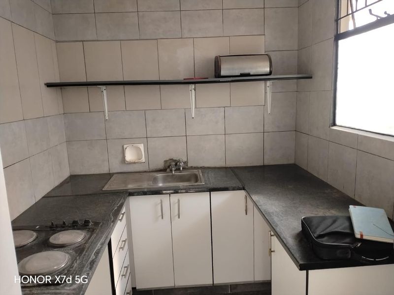 Compact kitchen featuring white cabinetry, dark stone countertops, an integrated electric hob, and tiled splashback with wall-mounted shelving.