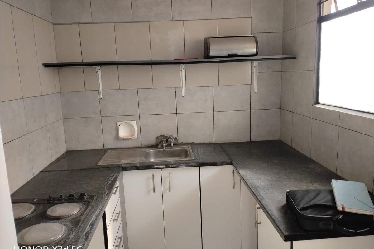 Compact kitchen featuring white cabinetry, dark stone countertops, an integrated electric hob, and tiled splashback with wall-mounted shelving.