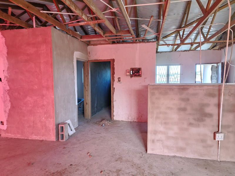 An open-plan interior space currently under construction, featuring exposed roof trusses, unfinished plastered walls, and basic electrical infrastructure.