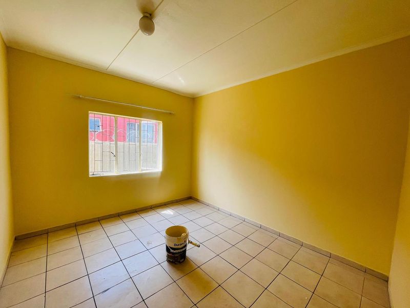 An empty bedroom featuring tiled flooring, a window with security bars, and a simple ceiling light fixture.