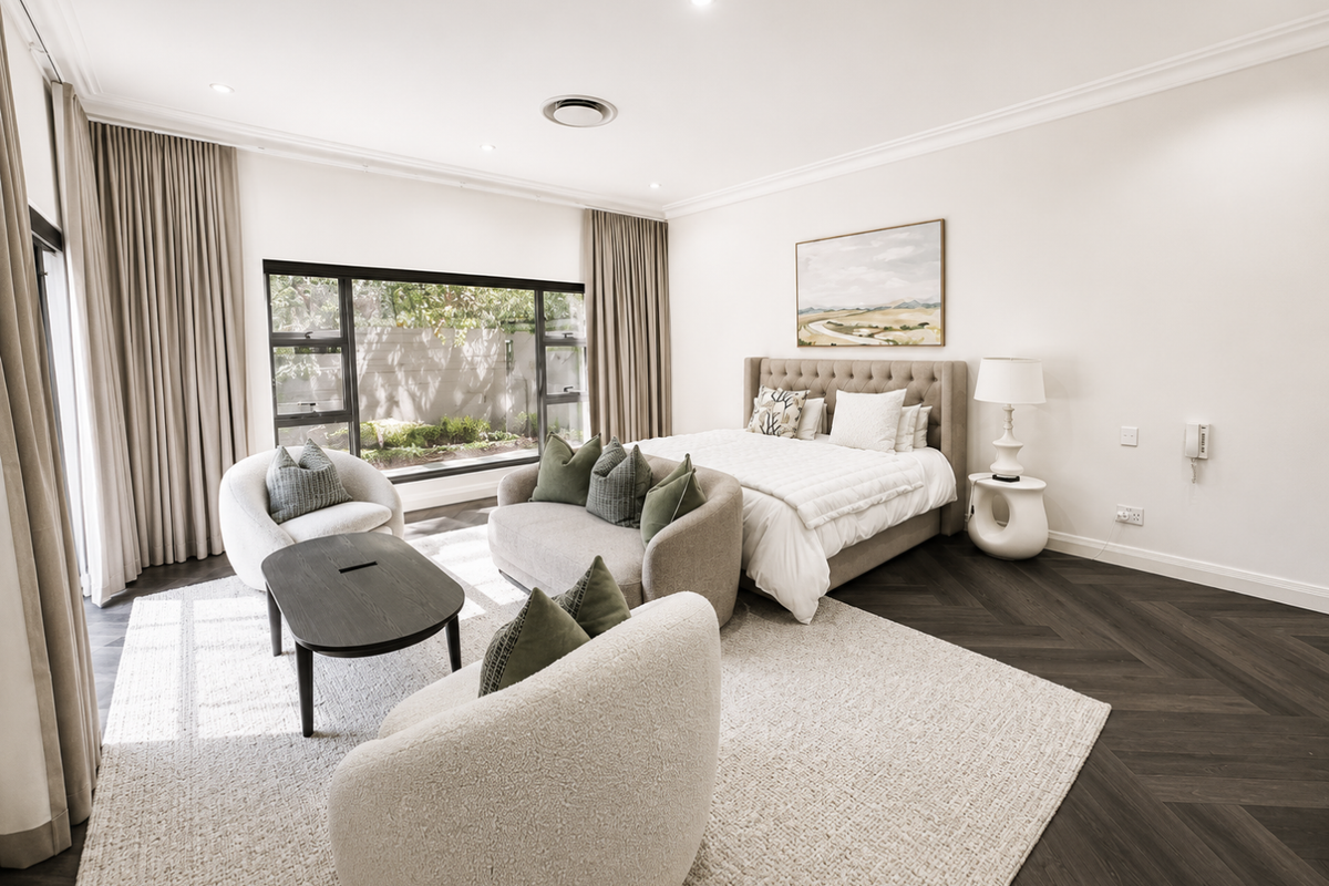 Spacious bedroom featuring elegant herringbone timber flooring, recessed downlighting, and a large window providing natural light and garden views.