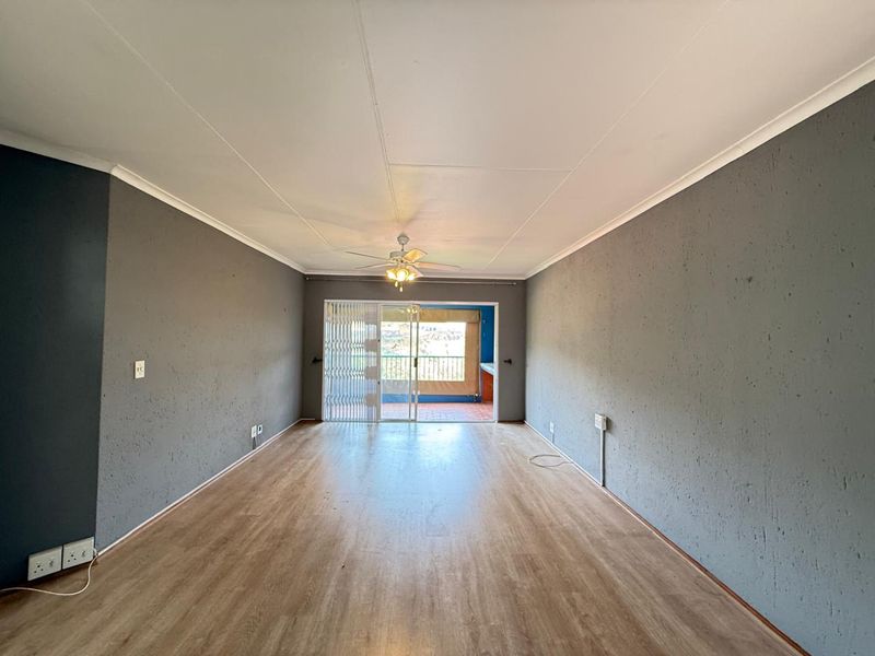 Spacious, empty living area featuring laminate flooring, a ceiling fan, and a sliding glass door leading to an outdoor balcony.