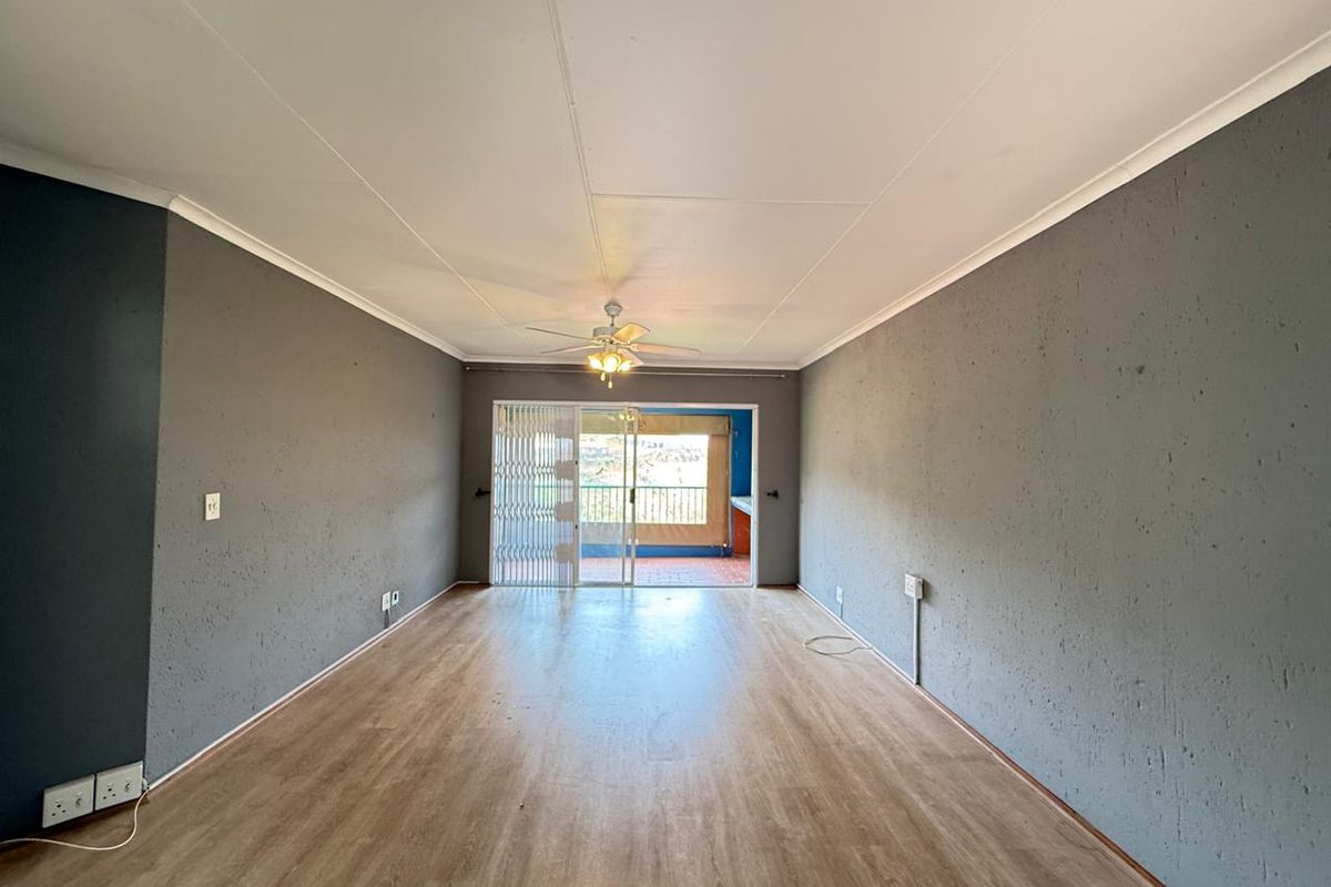 Spacious, empty living area featuring laminate flooring, a ceiling fan, and a sliding glass door leading to an outdoor balcony.