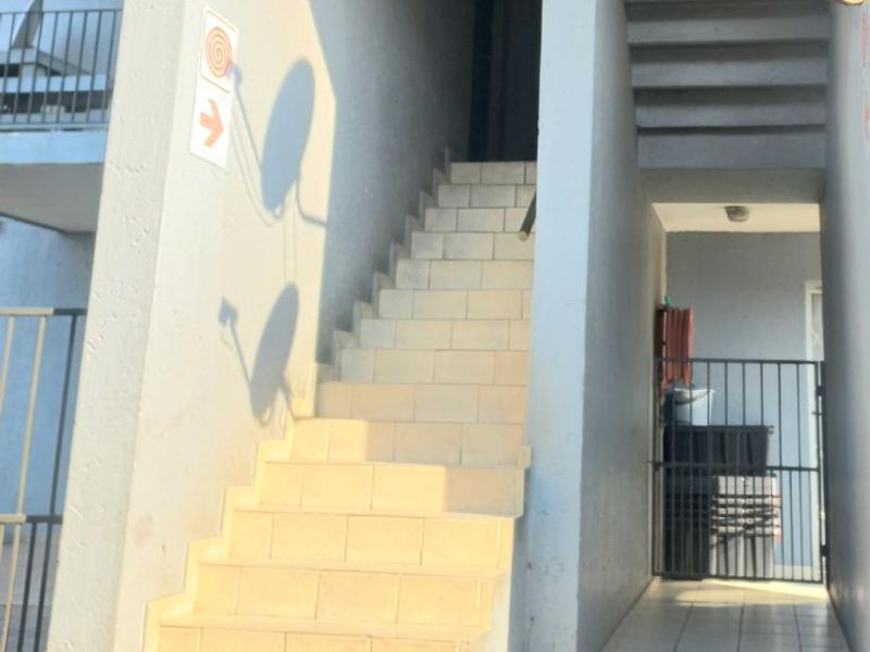 Exterior view of an apartment building entrance featuring a tiled staircase and metal security gate access.