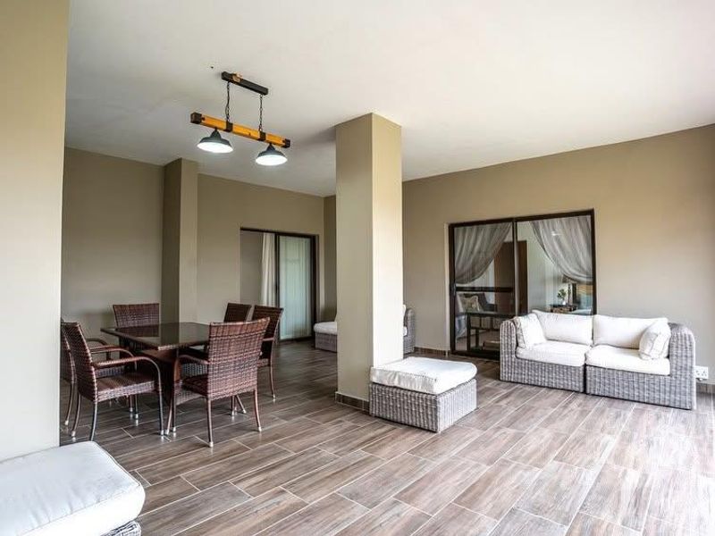 A spacious covered patio featuring wood-look tiled flooring, structural columns, and sliding glass doors providing seamless access to the interior living spaces.