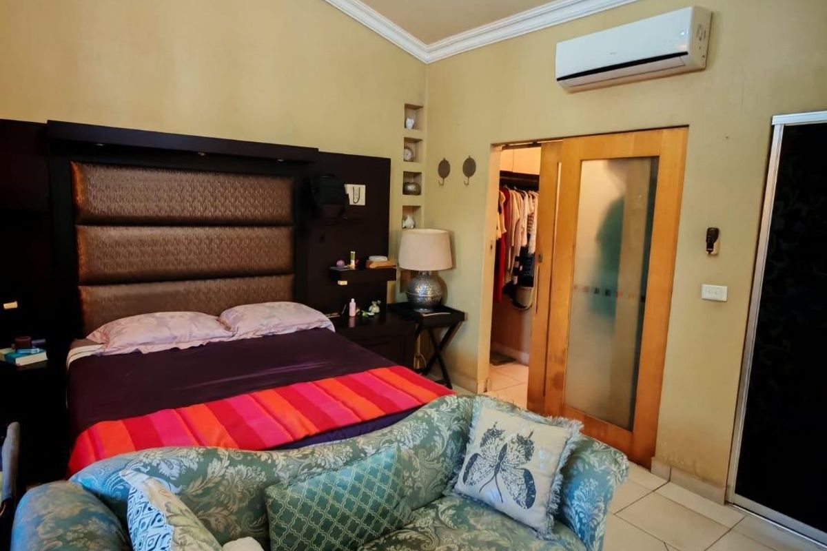 Spacious bedroom featuring a built-in headboard, split-system air conditioning, crown molding, and an adjoining walk-in closet with sliding door access.
