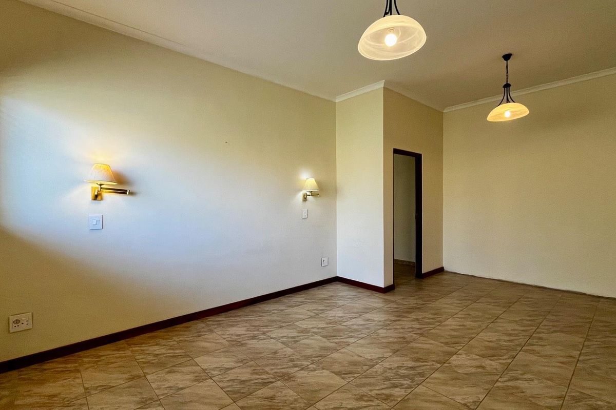 An empty living room featuring tiled flooring, wall sconces, and pendant lighting, providing a neutral and versatile space.