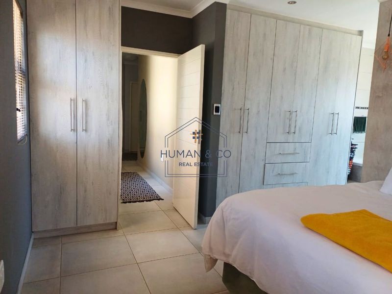 A well-maintained bedroom featuring extensive built-in cupboards with a modern wood-grain finish, neutral tiled flooring, and recessed ceiling lighting.