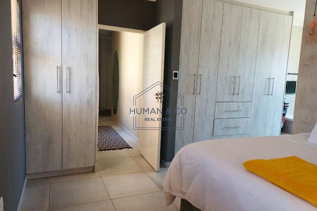 A well-maintained bedroom featuring extensive built-in cupboards with a modern wood-grain finish, neutral tiled flooring, and recessed ceiling lighting.