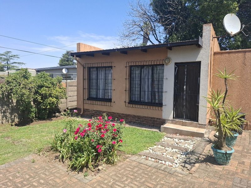 Rear view of a modest house featuring a paved walkway, small garden area, and security bars on the windows.