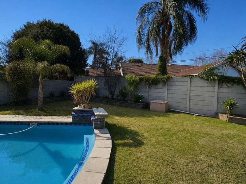 A well-maintained backyard featuring a swimming pool with tiled coping, surrounded by a lawn and a secure precast concrete boundary wall.