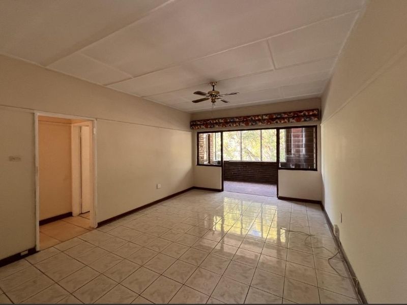 An empty, spacious living area featuring tiled flooring, a ceiling fan, and sliding doors leading to an outdoor balcony space.