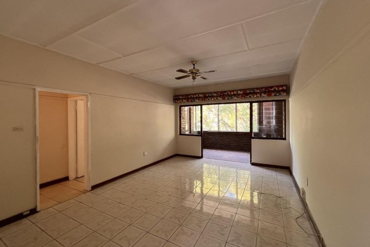 An empty, spacious living area featuring tiled flooring, a ceiling fan, and sliding doors leading to an outdoor balcony space.