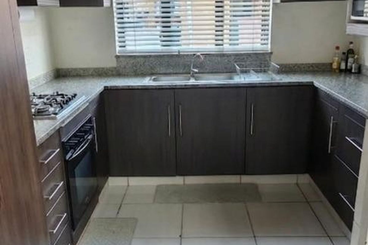 A functional kitchen featuring dark wood cabinetry, granite countertops, built-in oven, gas hob, and tiled flooring with a window providing natural light.
