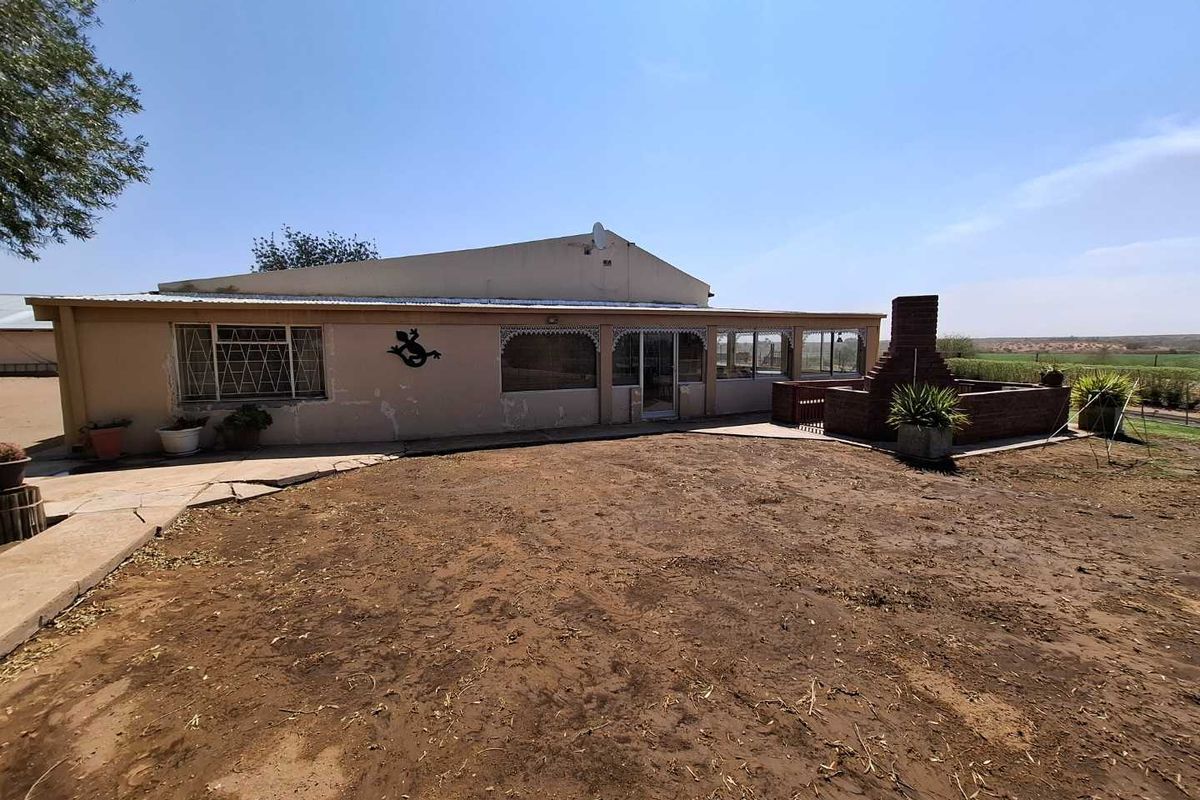 Rear view of the small holding featuring a covered patio area with a built-in brick braai and expansive surrounding grounds.