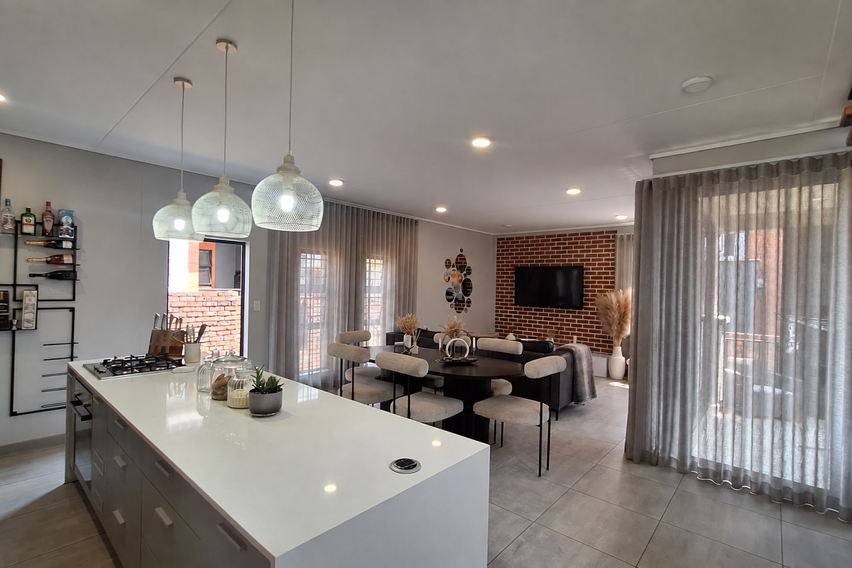 Modern open-plan living area featuring a sleek kitchen island with gas hob, exposed brick feature wall, and seamless flow to the dining and lounge space.