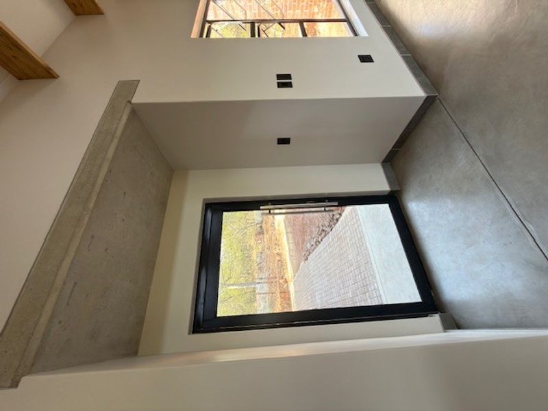 Modern entrance hall featuring polished concrete flooring, an exposed concrete beam, and large black aluminium framed glass door providing natural light.