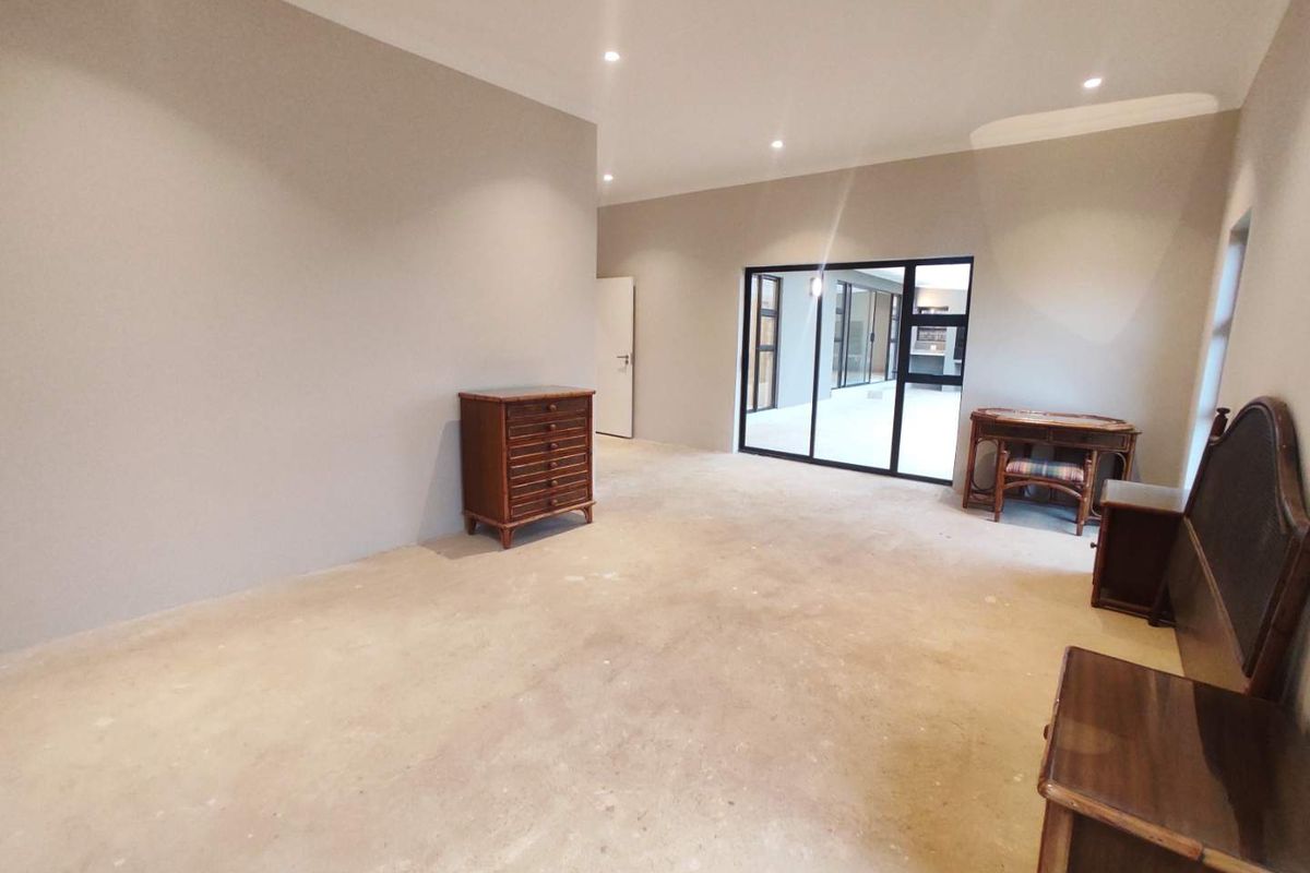 Spacious living area featuring recessed downlights, neutral walls, and large black aluminium sliding doors leading to an outdoor space, with unfinished concrete flooring.