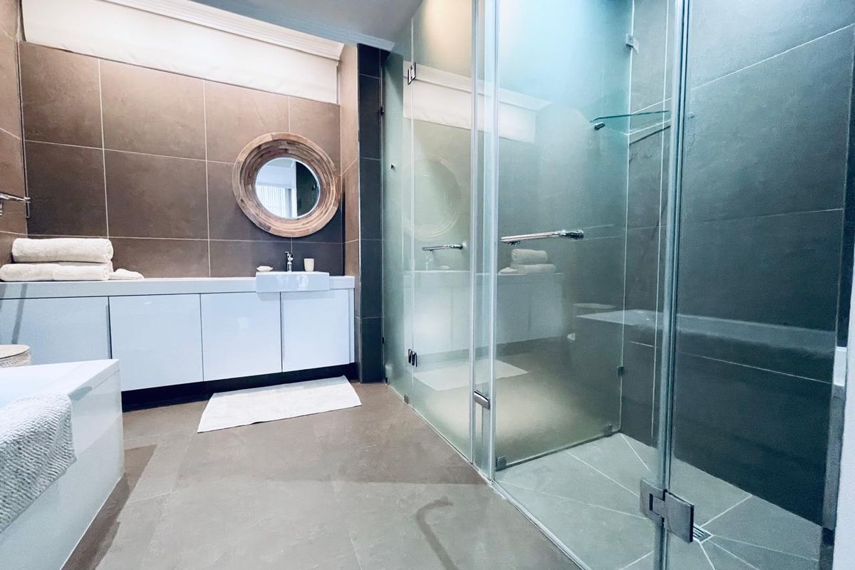Modern bathroom featuring a spacious walk-in glass shower, sleek vanity cabinet with integrated basin, and contemporary large-format wall and floor tiling.