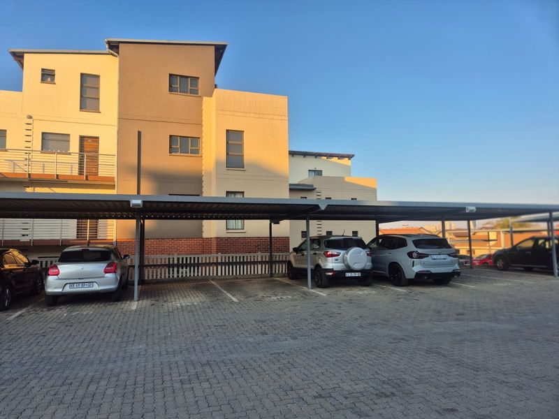 Exterior view of an apartment complex featuring a covered parking area with paved driveway and multi-story building facade.