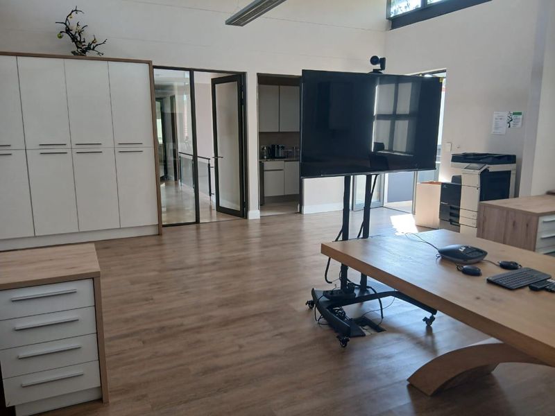 A modern, well-maintained office space featuring light wood-look flooring, built-in storage cabinetry, and glass-paneled doors leading to an adjacent area.