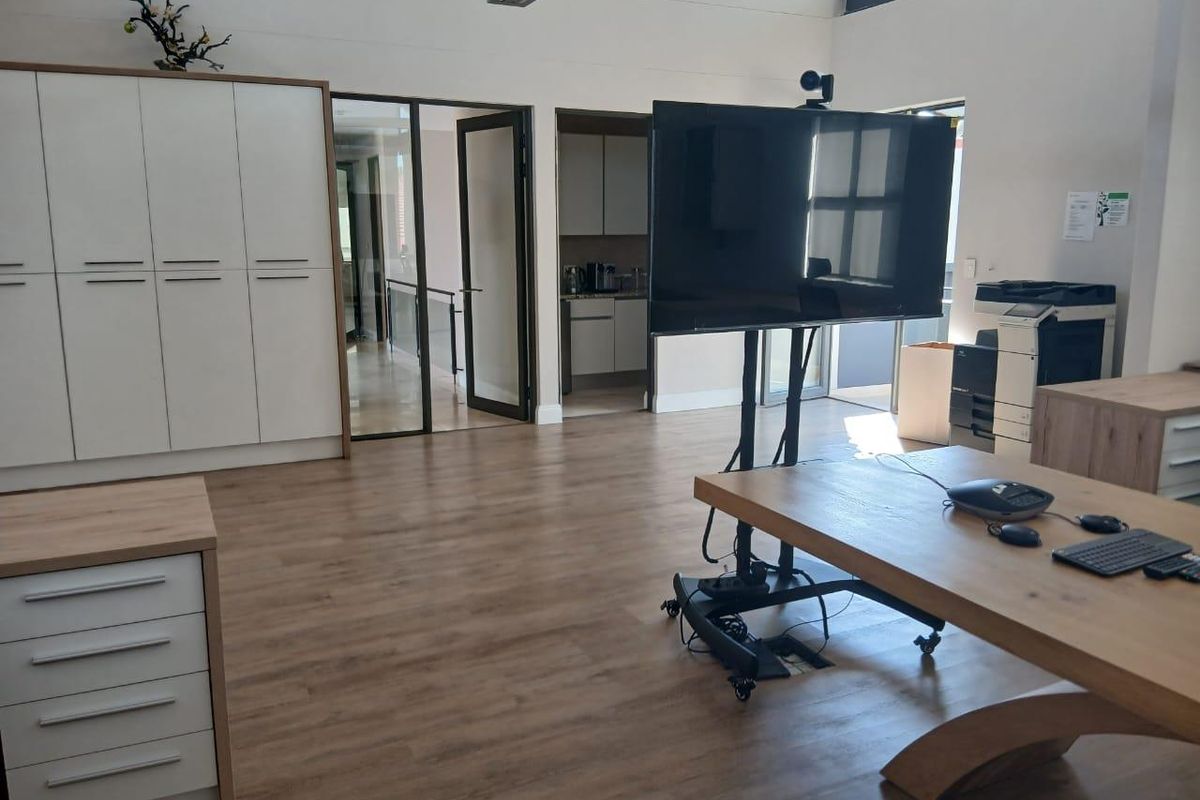 A modern, well-maintained office space featuring light wood-look flooring, built-in storage cabinetry, and glass-paneled doors leading to an adjacent area.