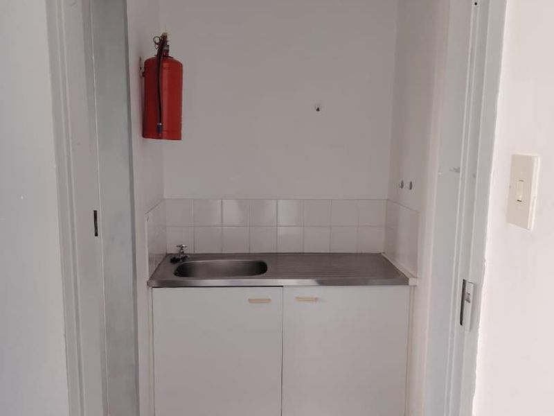 A compact utility or scullery area featuring a stainless steel sink, built-in base cabinetry, and a tiled splashback.