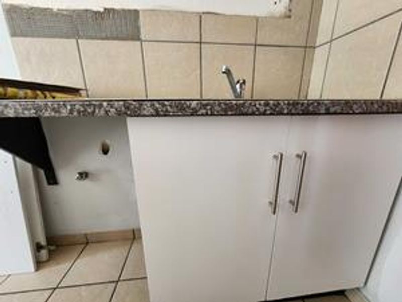 A small kitchen area featuring base cabinetry, a laminate countertop, and a sink faucet, currently requiring wall tiling and finishing work.