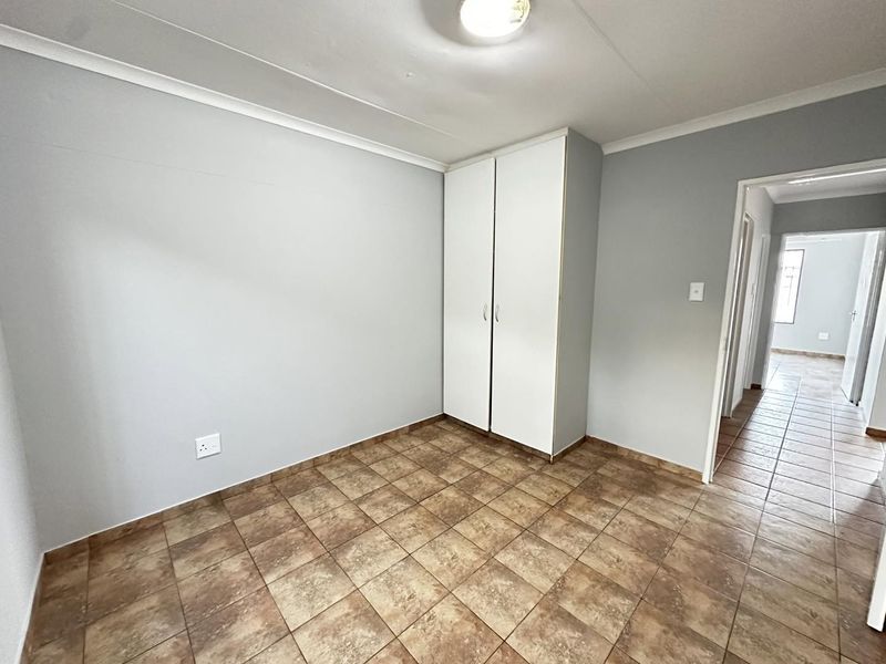 A clean, empty bedroom featuring neutral wall paint, tiled flooring, and a built-in wardrobe, offering a versatile space ready for personalization.
