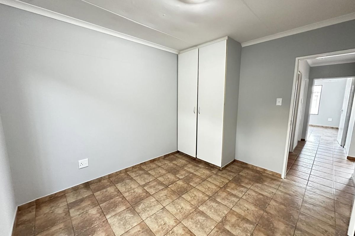 A clean, empty bedroom featuring neutral wall paint, tiled flooring, and a built-in wardrobe, offering a versatile space ready for personalization.