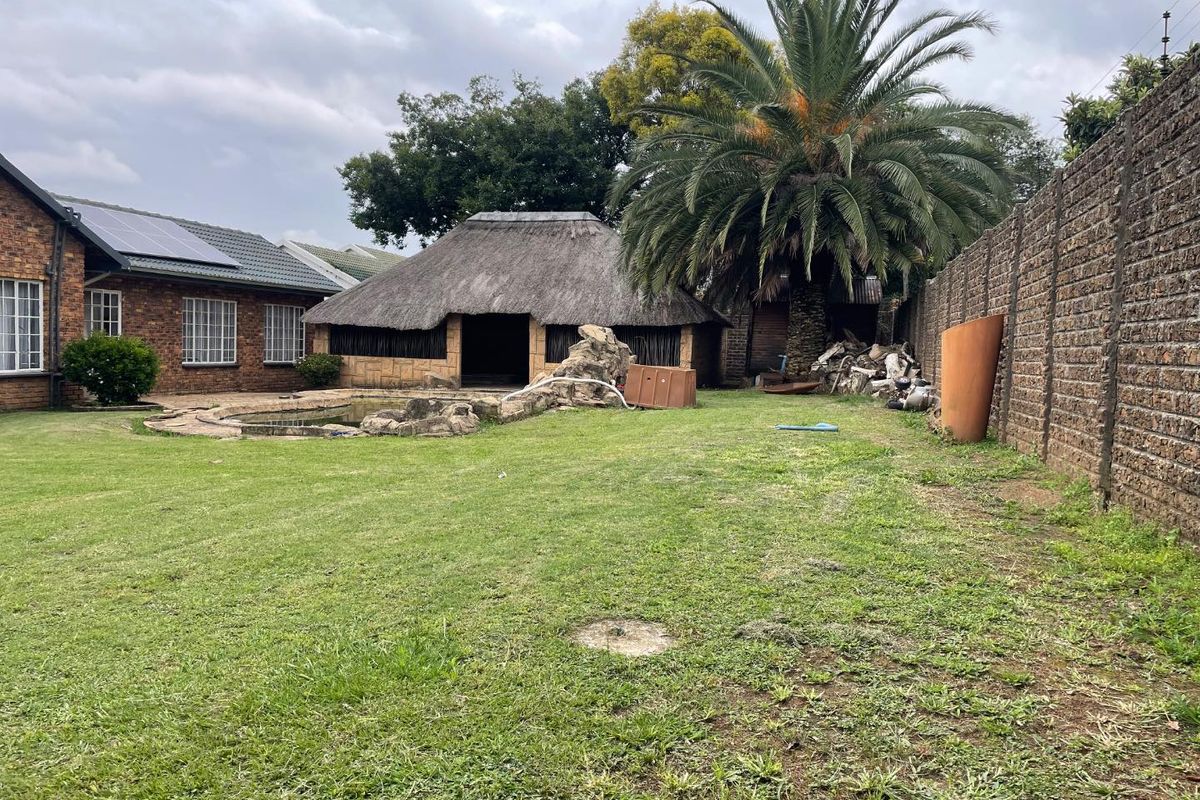 Spacious rear garden featuring a swimming pool, a traditional thatch-roofed lapa, and established palm tree, enclosed by a high brick boundary wall.